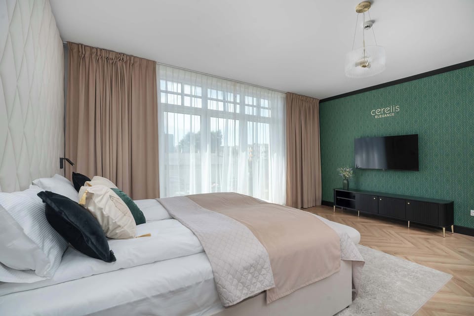 A side view of the bed highlights the crisp white linens, a decorative throw, and dark pillows. Large windows create a bright backdrop.