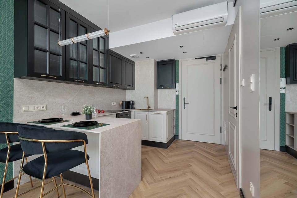 The entry flows past the kitchen, highlighted by dark glass upper cabinets. Two elegant blue bar stools stand at the breakfast counter.