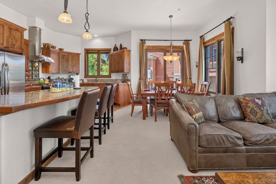 Relax in this inviting open-concept space where warm wood tones and comfortable seating invite you to unwind. Sunlight streams through large windows, highlighting the seamless flow from kitchen to dining to living areas—perfect for gathering.