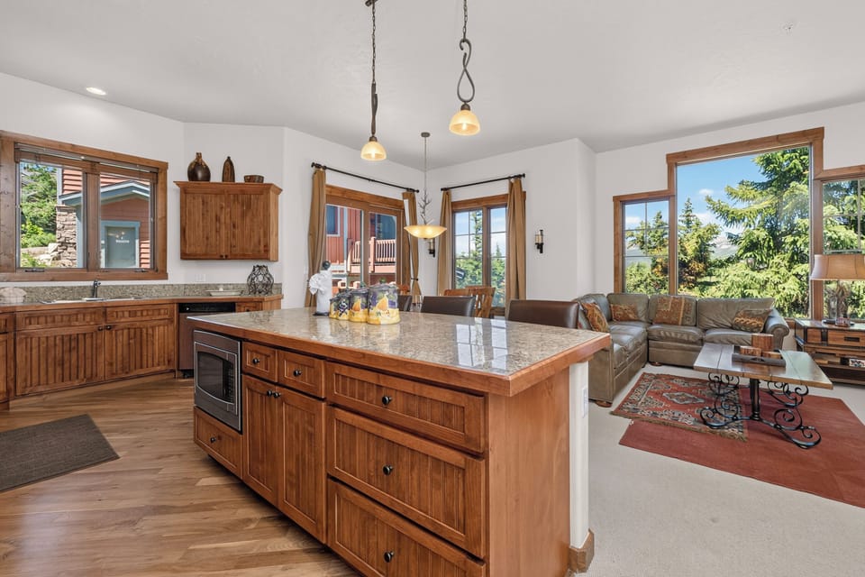 Your bright, open-concept living space seamlessly blends gourmet kitchen and cozy lounge, all framed by large windows inviting natural light and mountain views into every moment of your stay.