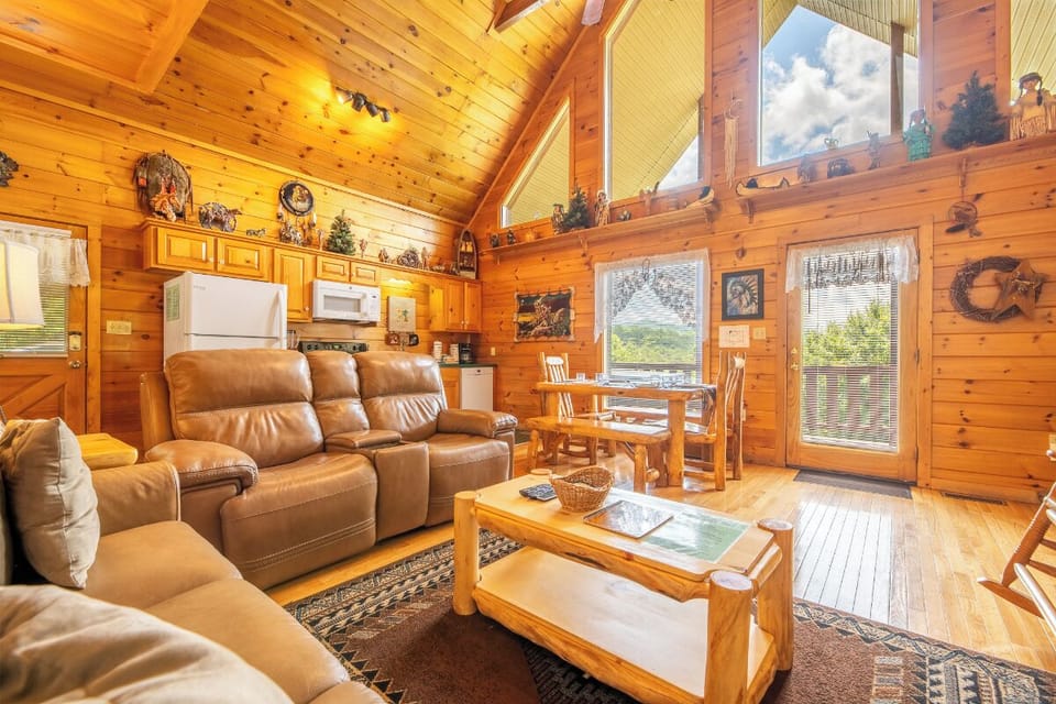 Step into your cozy mountain retreat, where warm wood walls embrace plush leather seating and rustic charm meets comfort. Sunlight pours through soaring windows, inviting you to unwind in your personal cabin sanctuary.