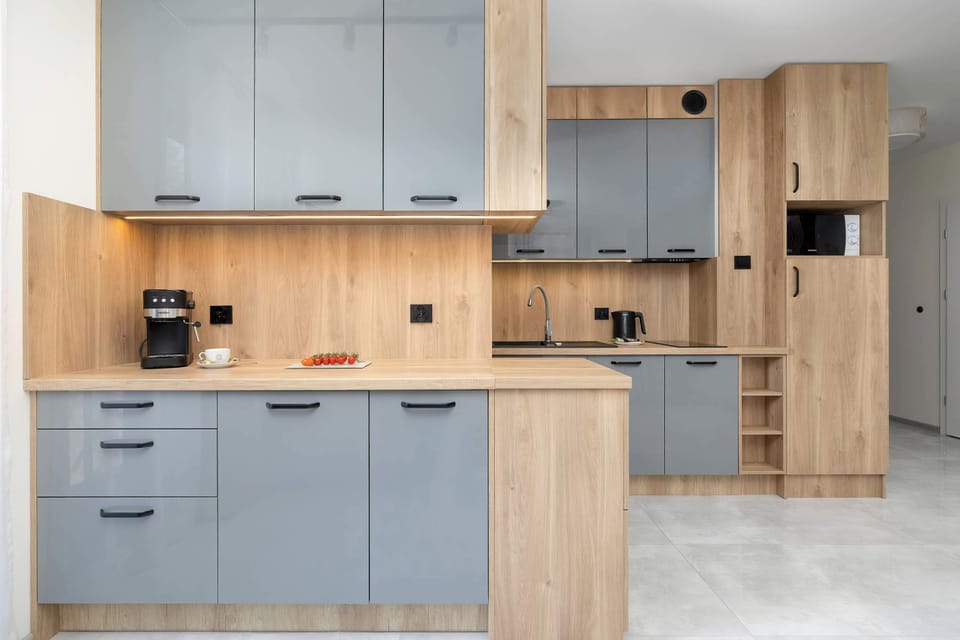 The kitchen counter features light grey cabinets below and above a warm wood-textured splashback. Integrated kitchen appliances look sleek.