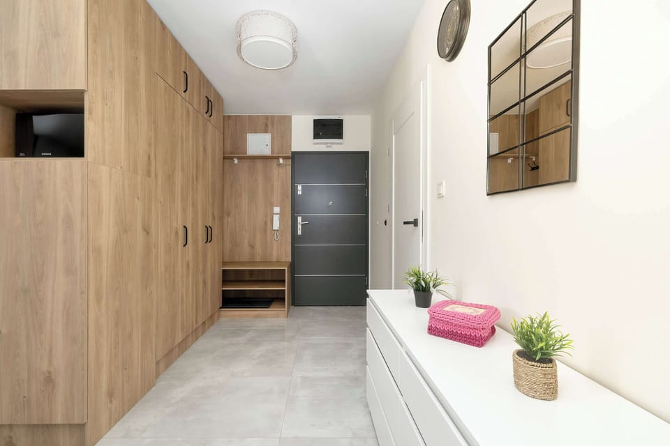 The entry hallway is lined with floor-to-ceiling wooden storage cabinets. A white dresser decorated with small plants stands on the opposite side.