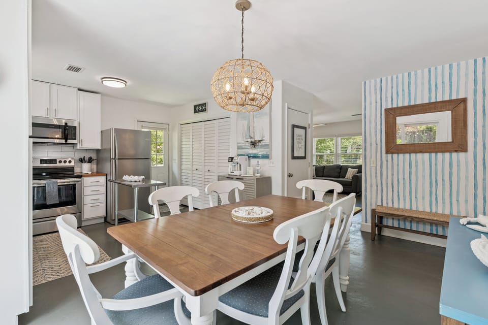 Gather around the warm wood dining table under coastal-inspired lighting, where your morning coffee and evening meals feel like home. The bright, beach-themed space connects seamlessly to your fully equipped kitchen.