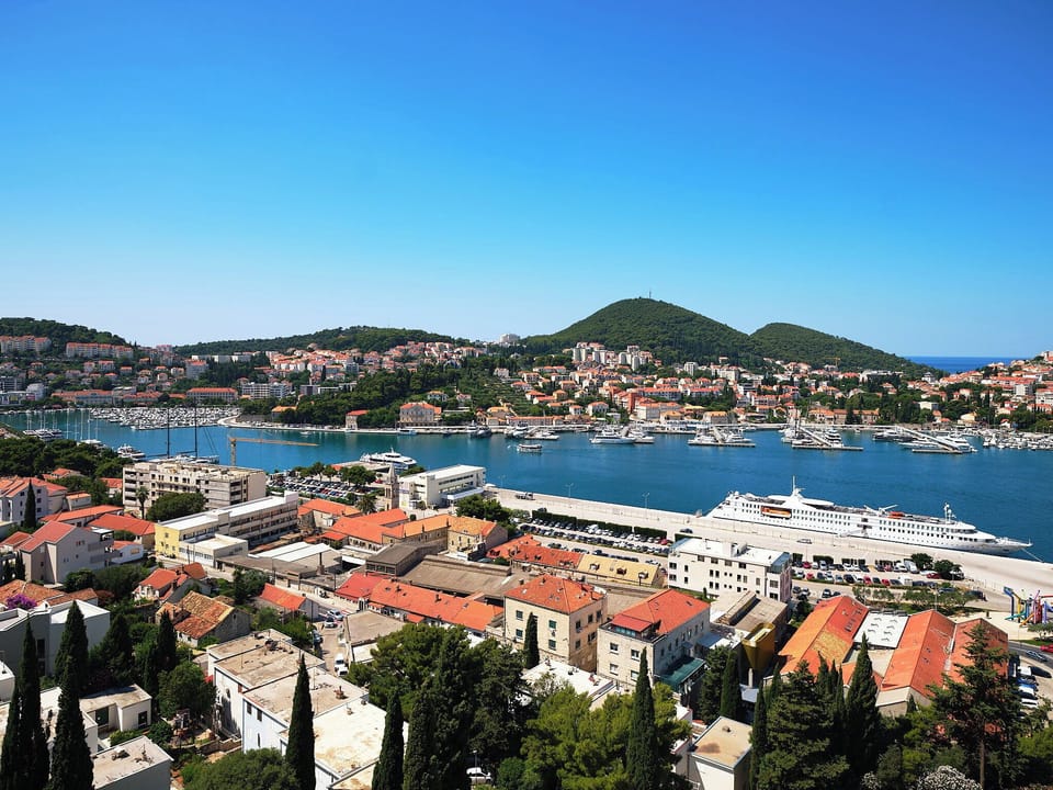 Marvel at panoramic views of Gruž Harbor's blue waters. Watch elegant cruise ships arrive past vibrant red-roofed homes.