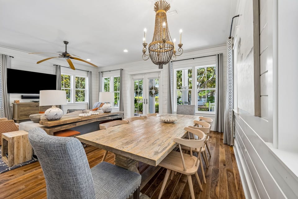 Gather around the handcrafted dining table beneath a stunning chandelier as natural light pours through French doors, creating a bright and airy space perfect for memorable meals with loved ones.
