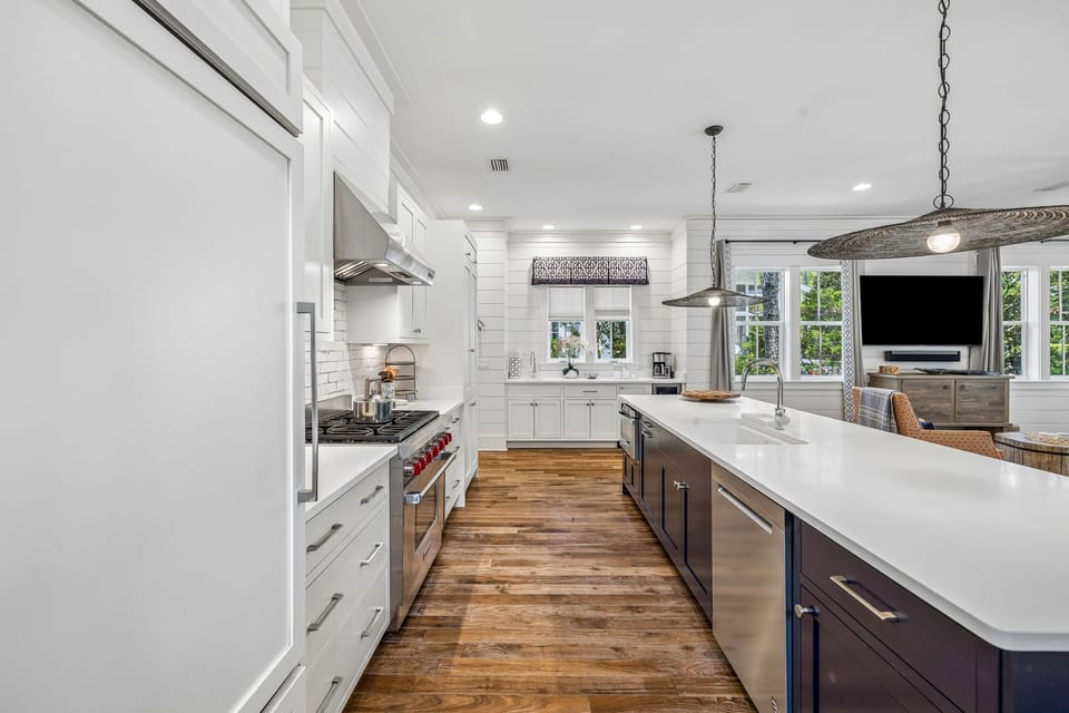 Picture yourself preparing meals in this bright, beautifully appointed kitchen with sleek white countertops and warm wood floors, where natural light streams through large windows and modern pendants add farmhouse charm overhead.