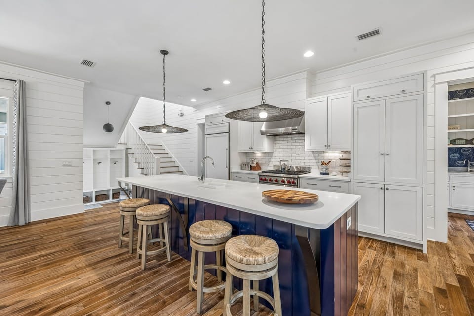 Your coastal-inspired kitchen combines modern elegance with homey charm—crisp white cabinets, a striking blue island with seating, and gleaming countertops perfect for cooking and gathering.