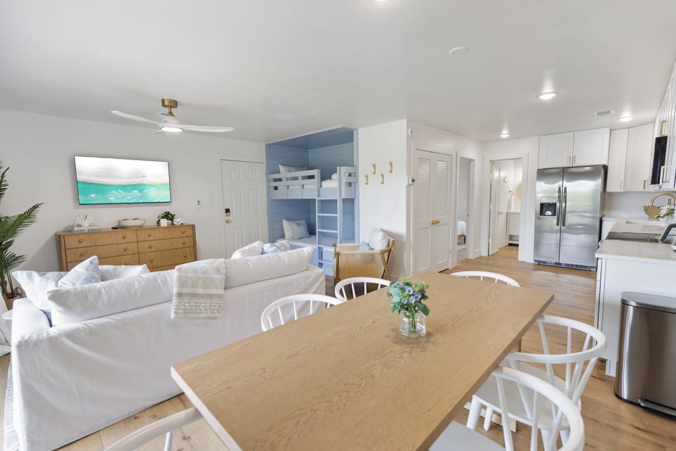 Picture yourself in this airy, coastal-inspired space with a fully equipped kitchen, cozy dining area, and inviting living room—all bathed in natural light and beach-view artwork.