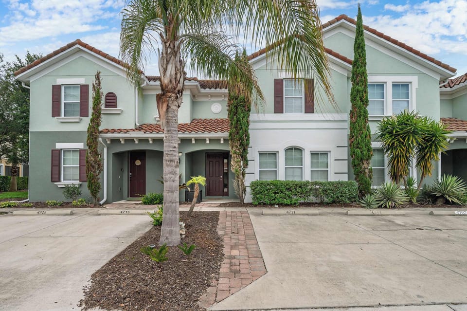 Exterior view of a modern townhouse with tropical landscaping and designated parking spaces.