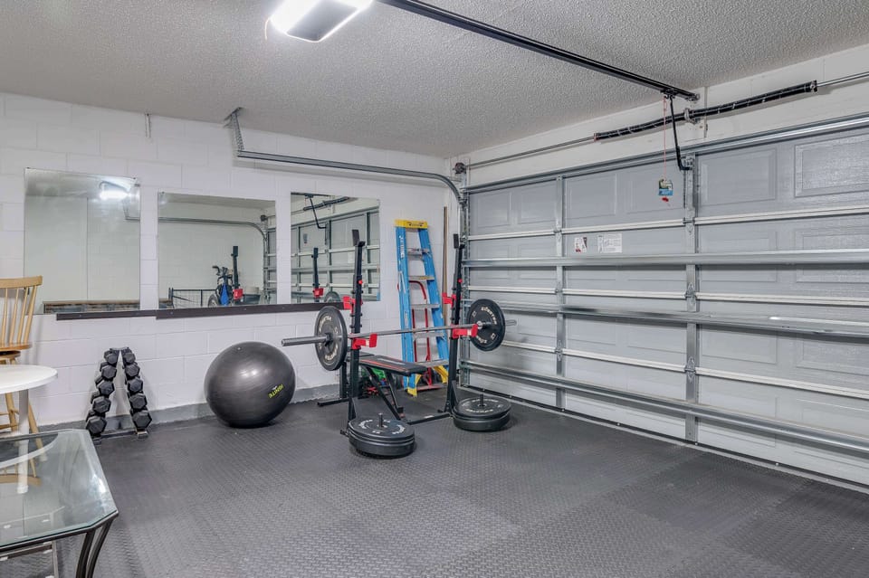 Home gym setup with weightlifting equipment and mirrors in a garage space.