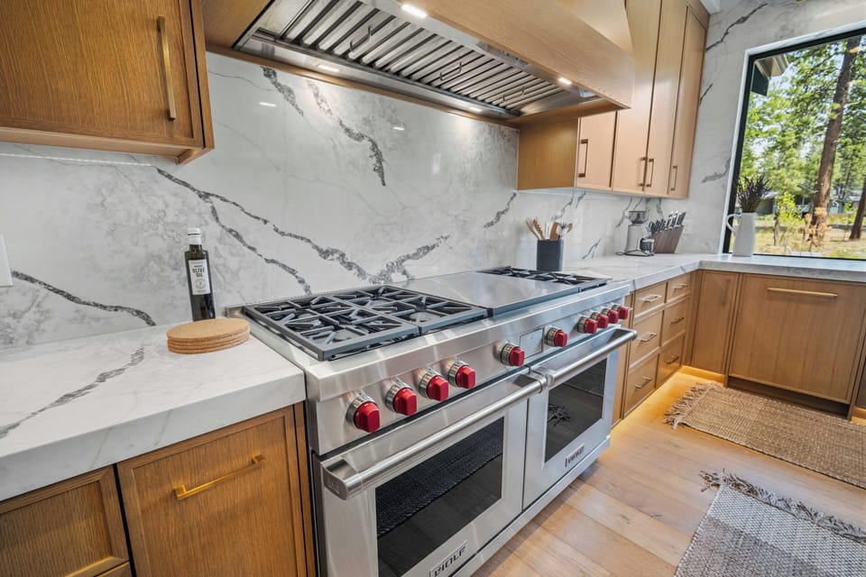 Your chef-inspired kitchen features a professional gas range with vibrant red knobs, elegant marble countertops, and warm wood cabinetry—perfect for preparing memorable meals during your stay.