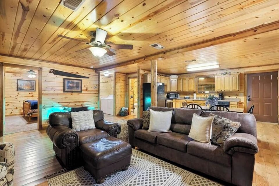 Sink into plush leather sofas in your open-concept cabin retreat, where rustic wood beams frame a cozy living space that flows seamlessly into a fully-equipped kitchen—your mountain home away from home.