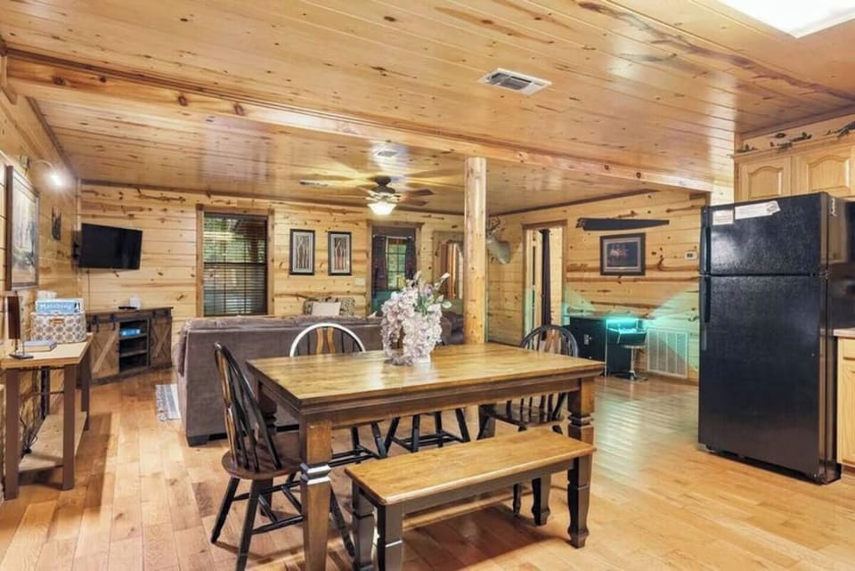 Warm wood-paneled open living space with dining area, kitchen, and cozy seating invites you to relax and gather under vaulted ceilings with rustic charm.