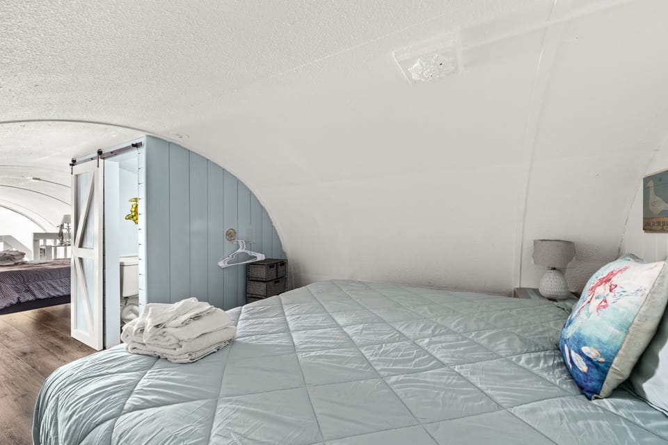 Drift off beneath the sloped ceiling in this cozy loft-style sleeping space with soft coastal colors and serene charm.