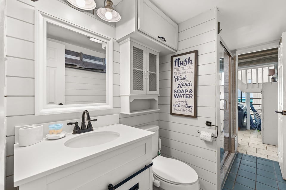 Your private bathroom features bright shiplap walls, crisp white countertops, and charming coastal touches. Soft lighting and a well-organized layout create a fresh, inviting retreat.
