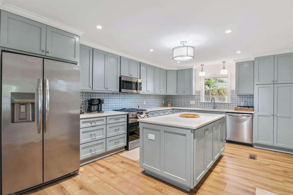 Your fully equipped kitchen features modern stainless steel appliances, elegant soft-gray cabinetry, and a spacious island perfect for meal prep or casual dining together.