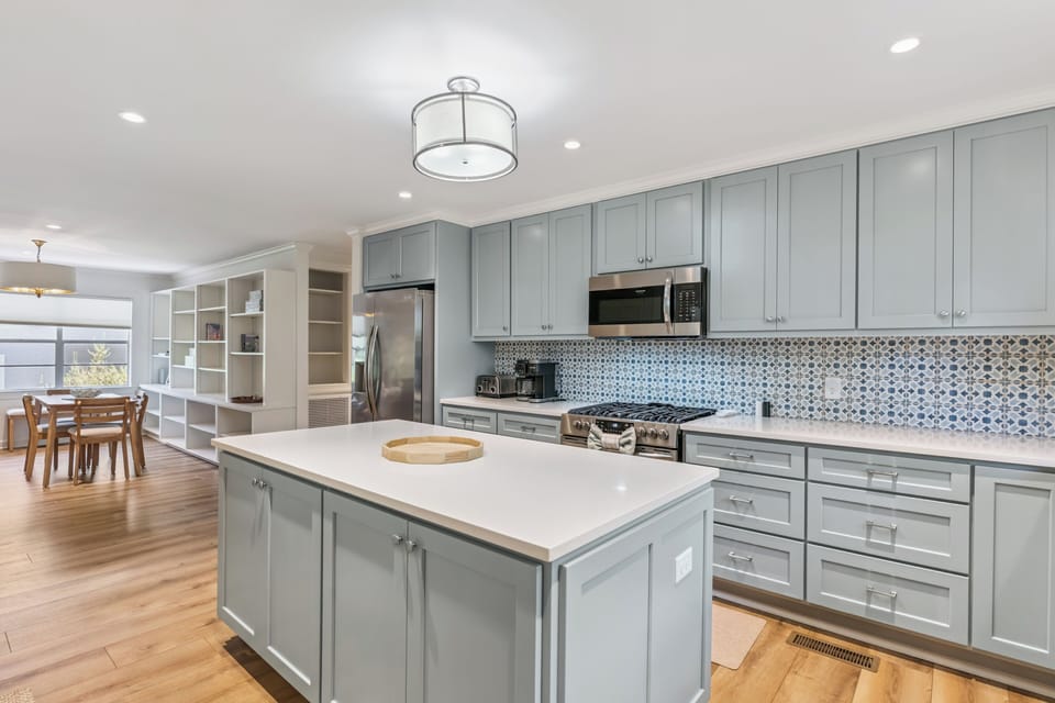 Step into your chef's dream: spacious kitchen with an elegant island, modern appliances, and charming blue-gray cabinetry bathed in natural light for memorable meals together.