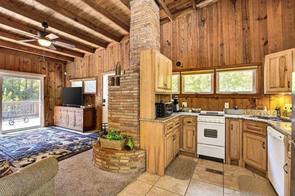Open kitchen and living area with wood-paneled walls, brick chimney, and sliding doors to the back deck.