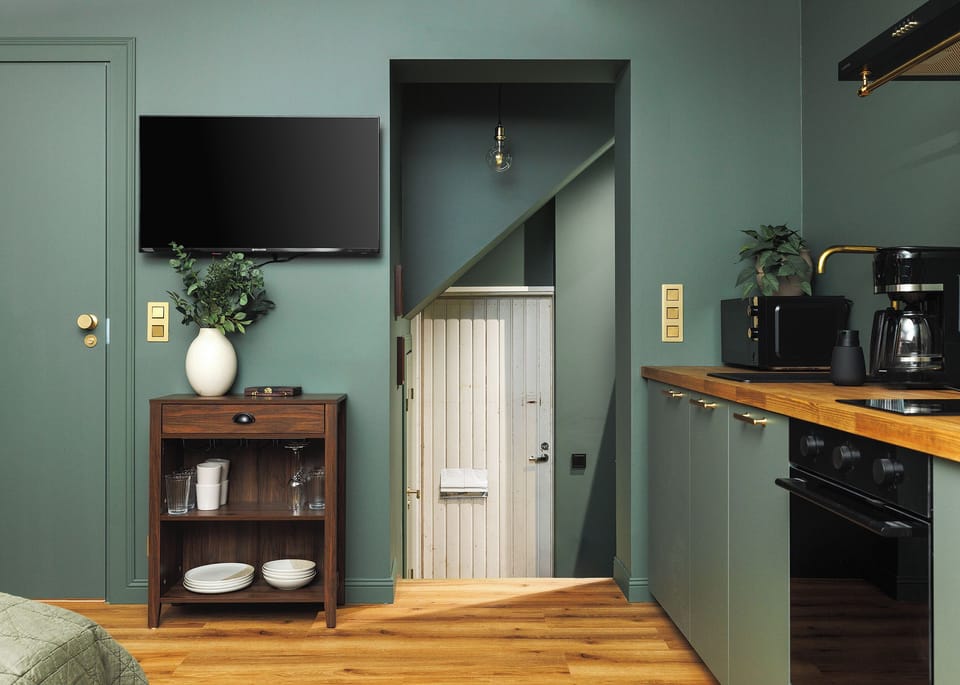 Chic sage-green architectural studio with kitchen, TV, and warm wood accents