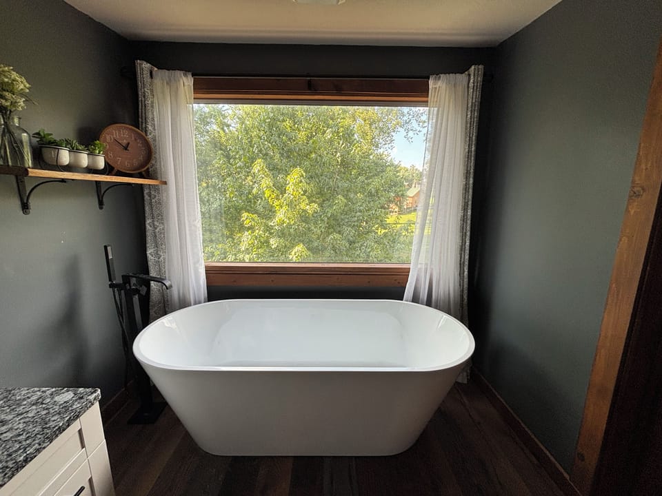 Spa-like soaking tub with large picture window and peaceful treetop views