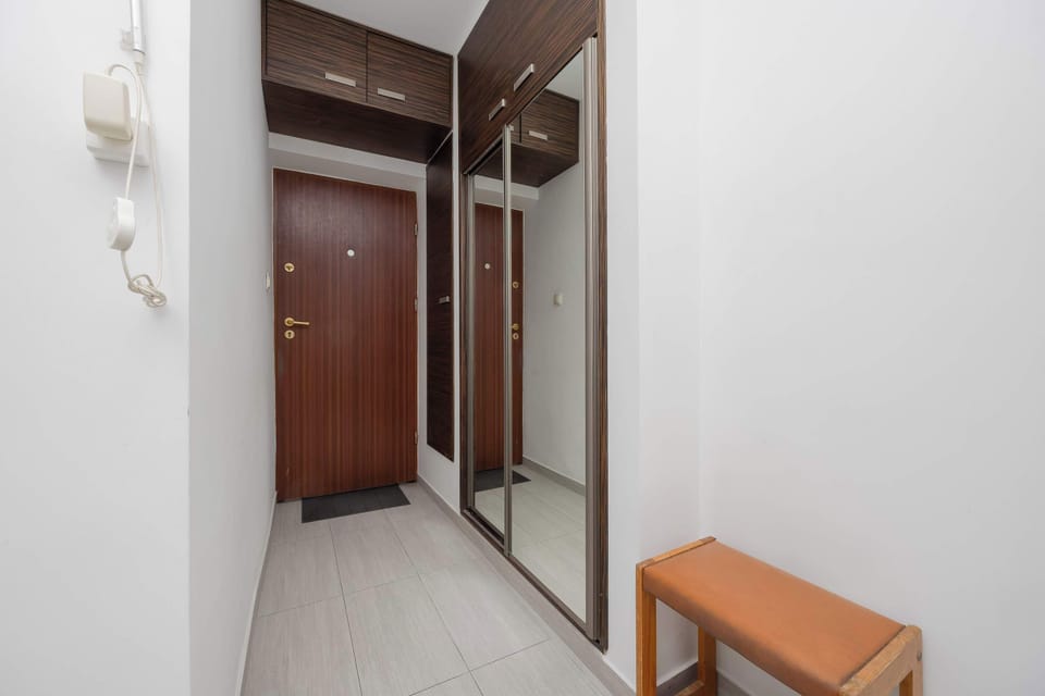 A simple hallway with wooden entrance doors and a small bench. The space has a clean and modern design.