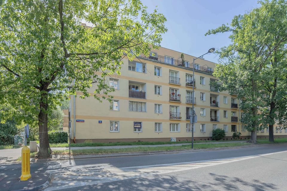 An exterior view of the apartment building surrounded by mature trees. The quiet residential setting provides a peaceful environment.