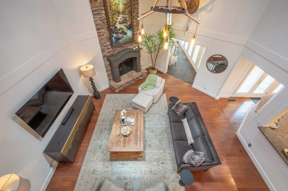 An overhead view of the living room. Featuring a stone fireplace, hardwood floors, a large area rug, and an expansive seating arrangement.