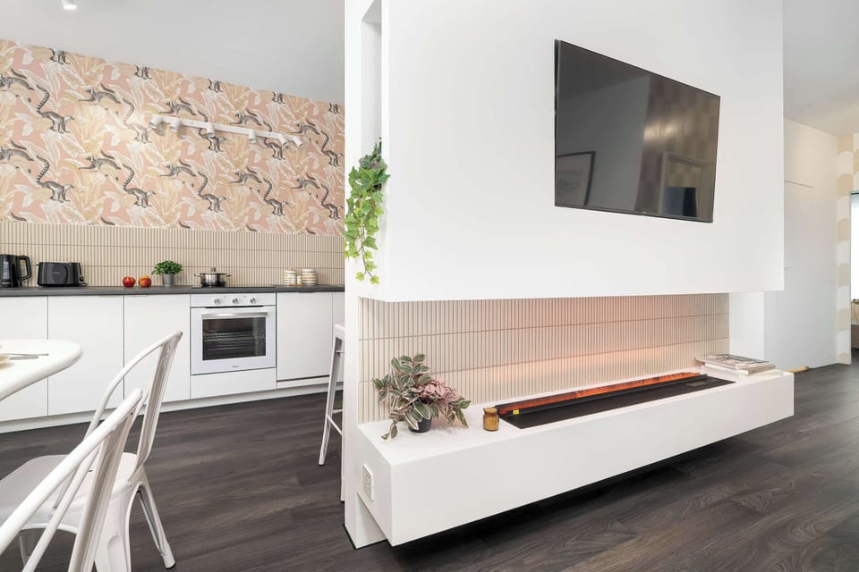 A wide-angle view reveals the seamless flow between the white kitchen and the adjacent living zone. The unique patterned kitchen backsplash serves as a focal point in the open layout.