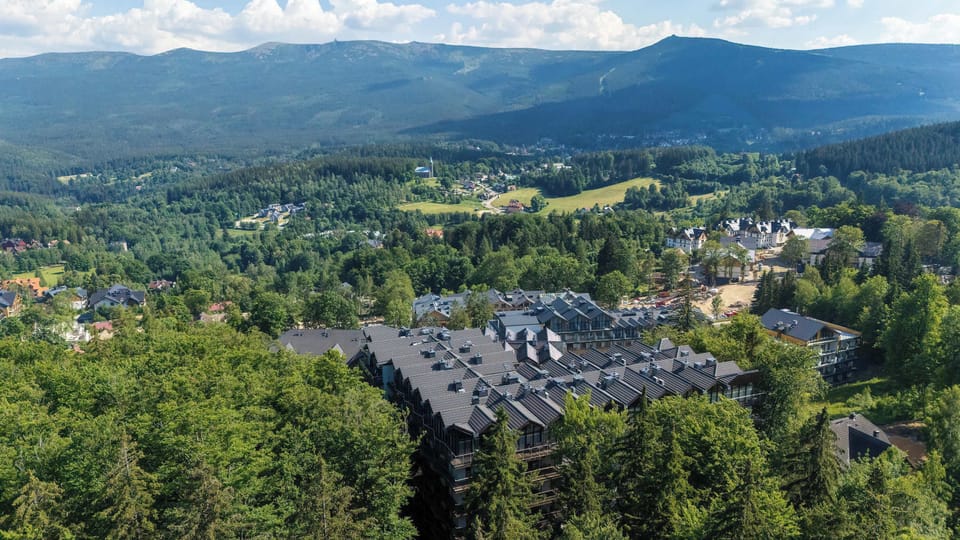 An aerial view shows the apartment complex surrounded by forests and mountains. The location offers beautiful natural scenery.