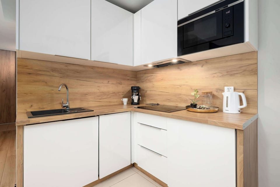 A modern kitchenette with white cabinets and wooden countertops. The space is bright and fully equipped for cooking.