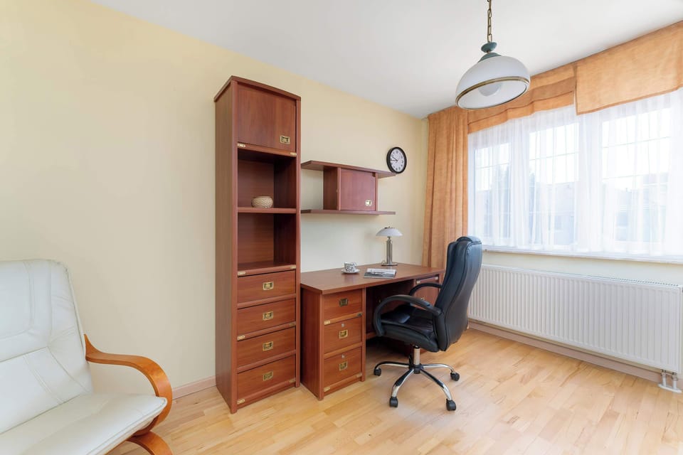 A compact bedroom with a desk, armchair, and wooden flooring. Simple furnishings keep the space uncluttered.