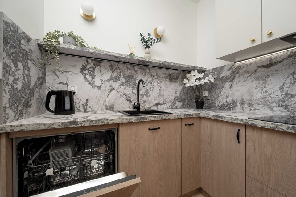 A closer look at the kitchen workspace reveals an integrated dishwasher hidden behind a wooden panel. The dramatic grey and white marble veins on the backsplash serve as a stunning focal point.