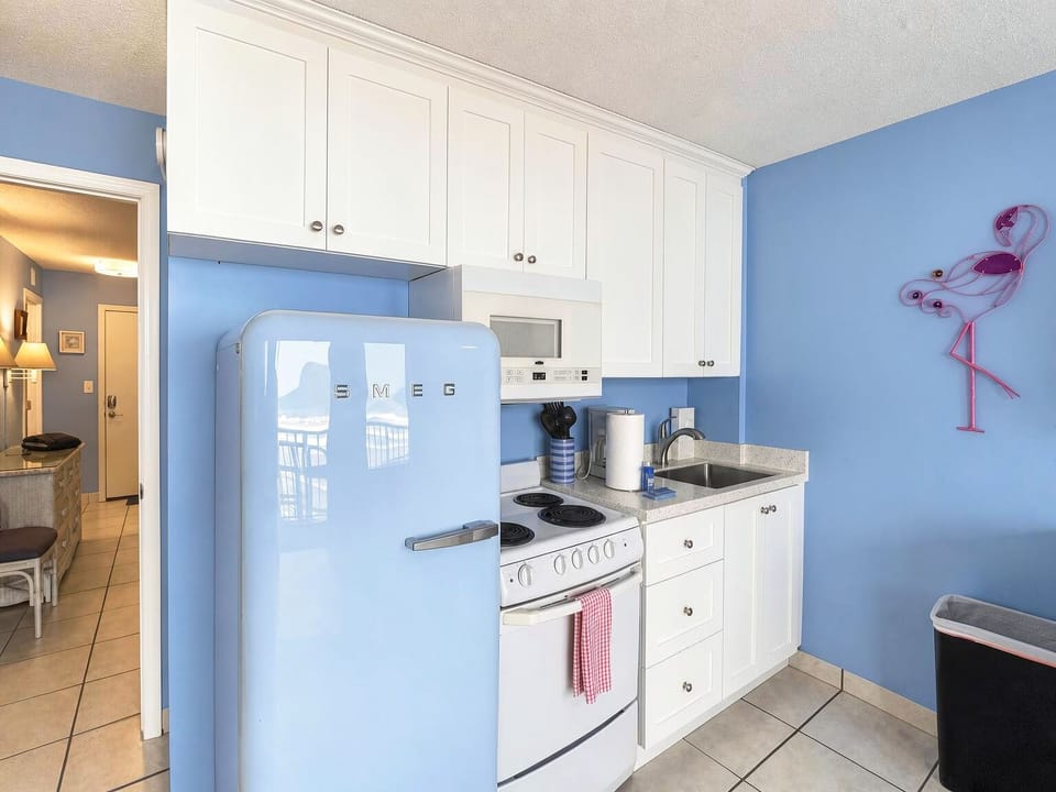 Your kitchen pops with cheerful retro style, featuring a vintage-inspired powder-blue fridge and bright coastal walls. Crisp white cabinets, a full stove, and modern touches make cooking a breeze in this fun, functional space.