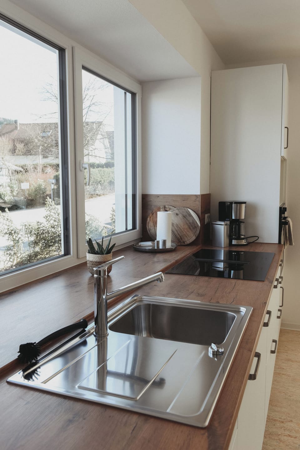 Sunlit, modern kitchen with induction cooktop, large sink, and coffee maker.