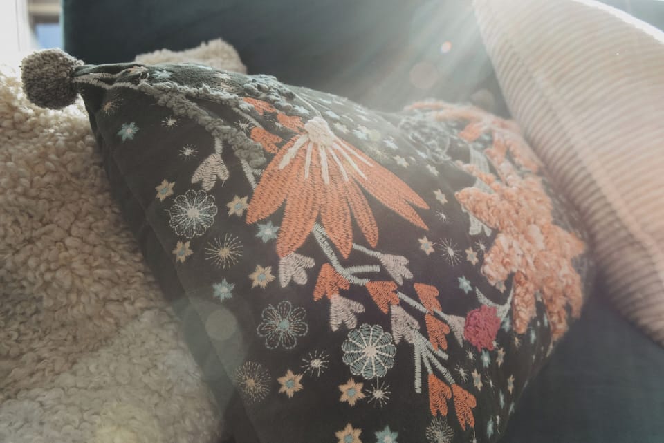 Sunlit sofa with embroidered pillows and cozy textures—relax here.