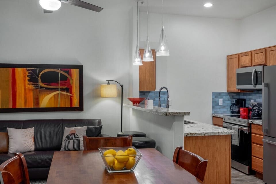 Open-concept living, dining, and kitchen with a wood dining table, leather sofa, and breakfast bar all in one bright, connected space