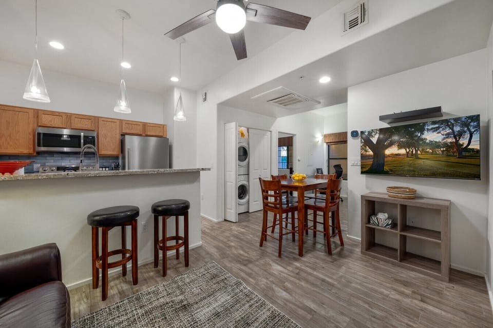 Bright, open floor plan connecting the living room, dining table, and kitchen — complete with a smart TV and in-unit washer/dryer