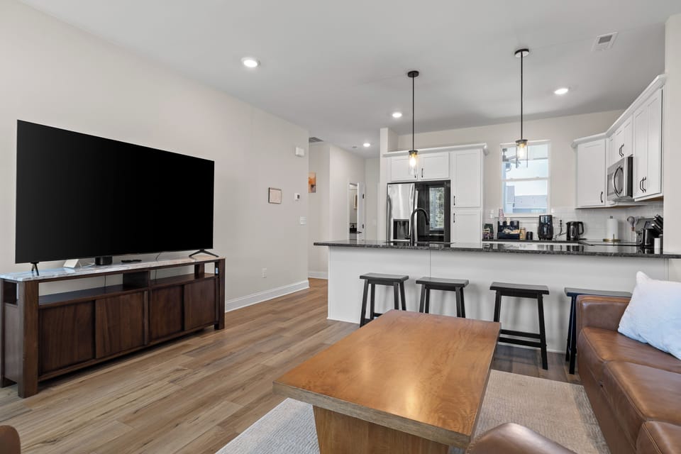 Bright open living space with modern kitchen, breakfast bar, and big TV