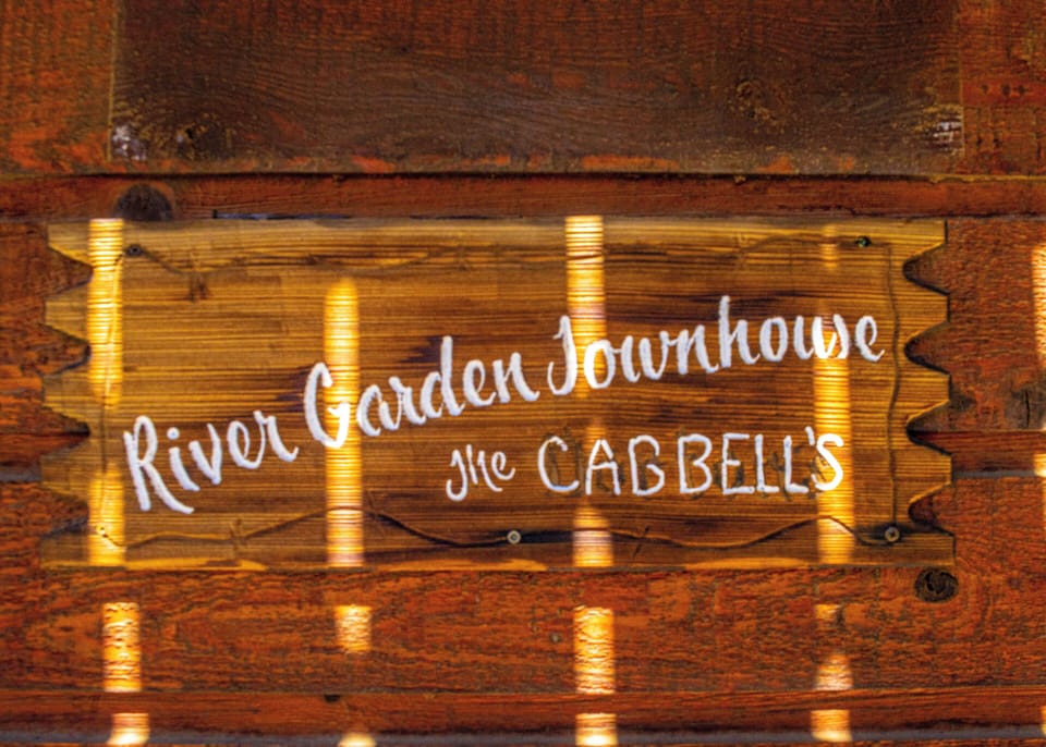 River Garden Townhouse welcomes guests with a warm, rustic wooden sign marking the entrance to the Cabbell's charming property.