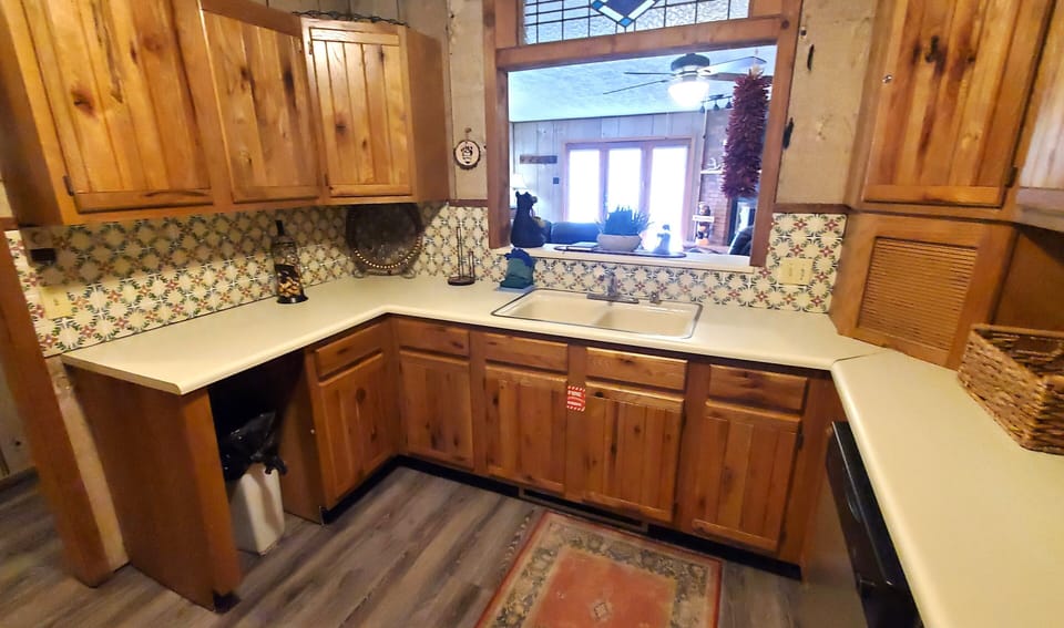 Your fully equipped kitchen invites home-cooked meals with warm knotty pine cabinetry, decorative tile backsplash, and ample counter space for meal prep. Natural light flows through the pass-through window, creating a welcoming culinary retreat.