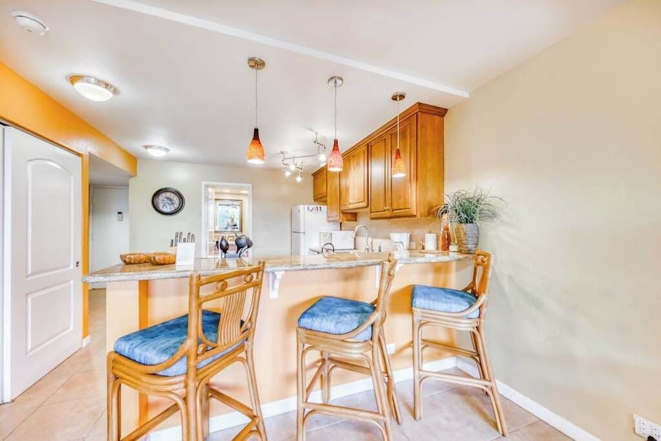 Spacious kitchen island breakfast bar featuring three wooden barstools with bright blue cushions and elegant overhead pendant lighting! 🍳🪑✨🌴