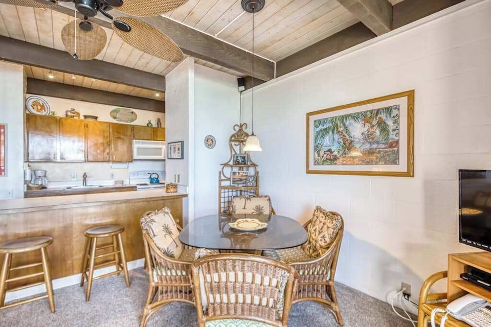 Spacious dining area featuring a woven table set, framed artwork, and an open kitchen breakfast bar with wooden counter stools! 🍽️🪑✨🌴😎
