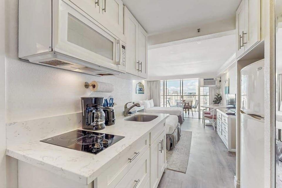 An efficient kitchenette comes equipped with an electric cooktop, microwave, coffee maker, and refrigerator.