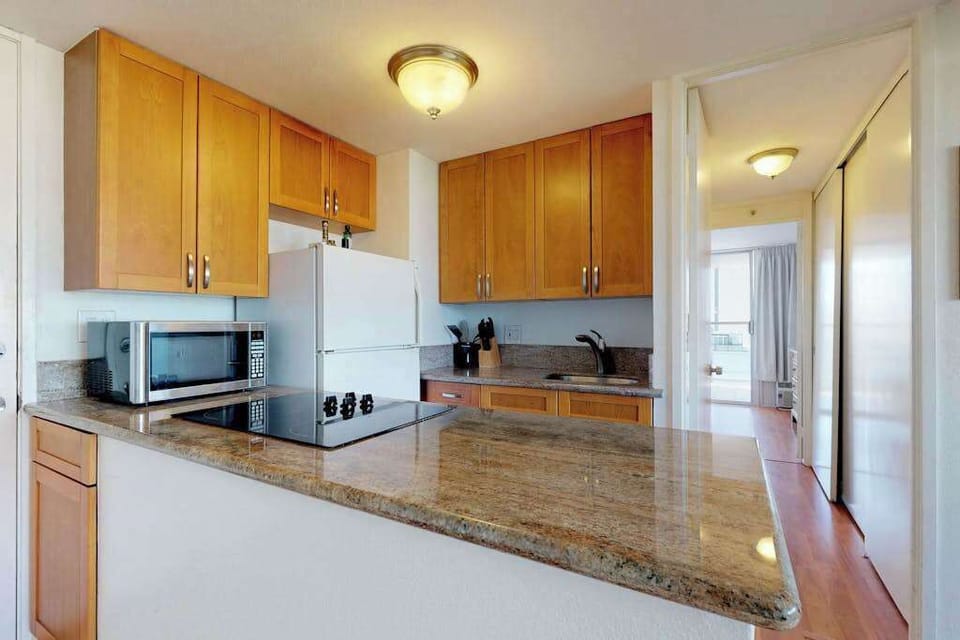 The convenient cooking area includes a flat-top electric stove and a microwave, seamlessly connecting to a hallway that leads through the unit.