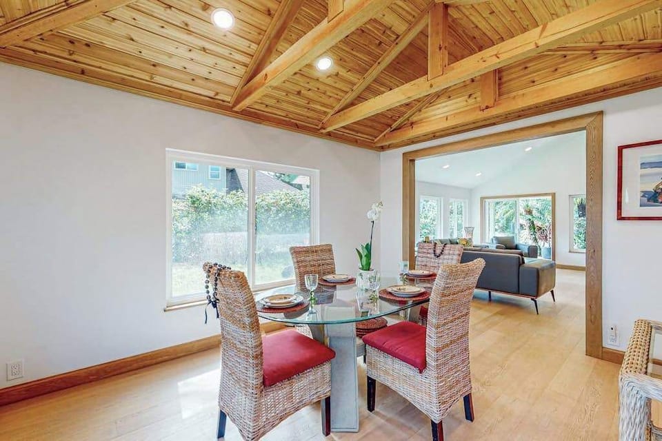 Dining table sits beneath wood beams with bright garden views beyond