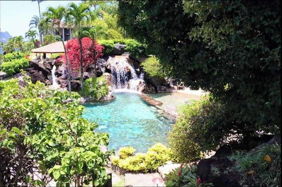 Waterfall flows through lush greenery, rocks, and peaceful landscaping