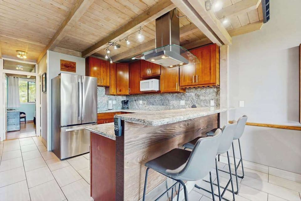Modern kitchen features wood cabinetry, island seating, and stainless appliances