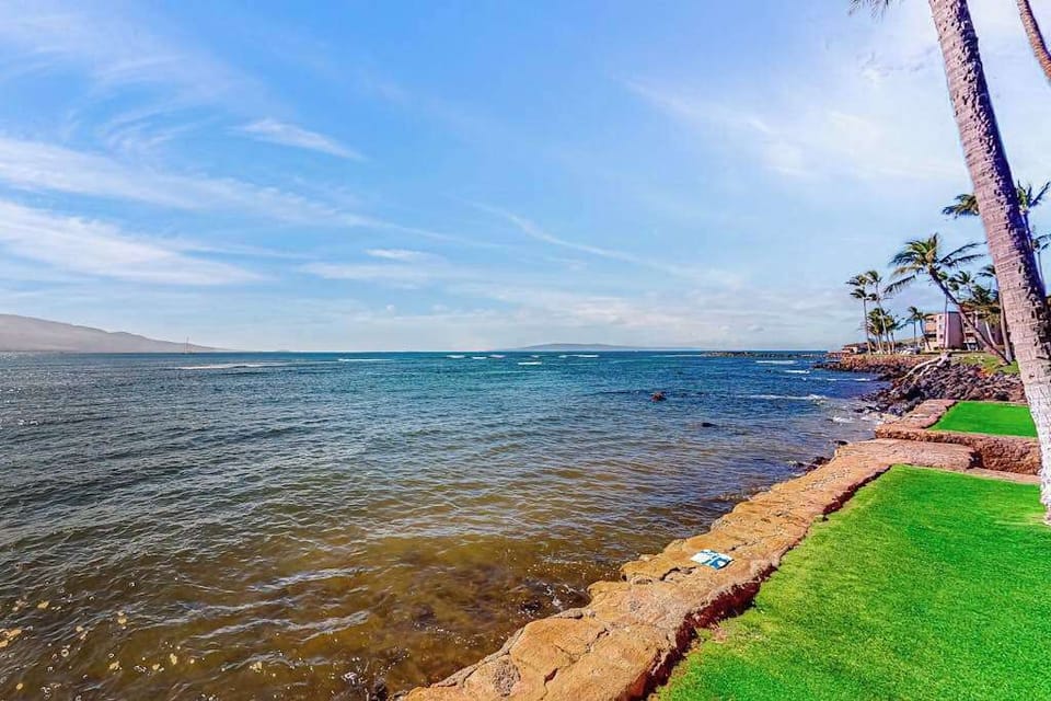 Oceanfront manicured lawns, swaying palm trees, and turquoise Pacific waters create a picture-perfect setting as waves gently crash along the shoreline.