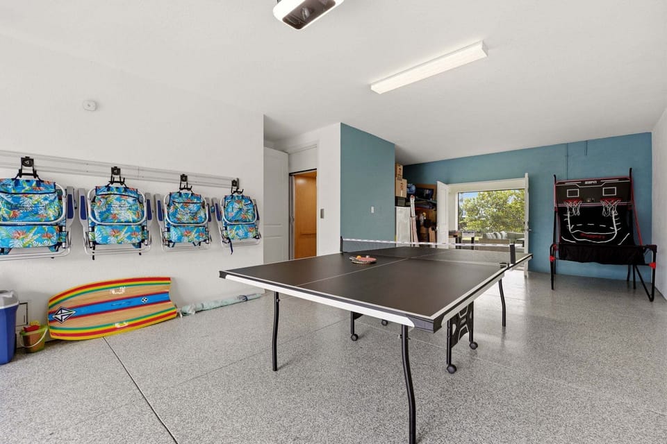 A second angle of the game room highlights the ping pong table, ESPN basketball shooter arcade game, and an open door leading directly to the enclosed ground-floor lounge.